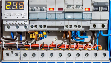 Gray and white electrical panel with digital display showing ’2.18’’ and multiple circuit breakers, wires in blue, orange, brown, and black colors neatly organized with yellow tags.